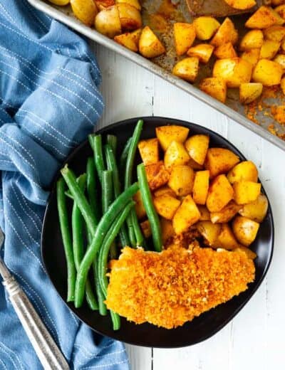 chicken, potatoes and green beans on a plate next to a blue napkin