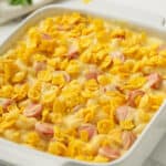 adding corn flakes to dish to make Mac and Cheese Hot Dog Casserole