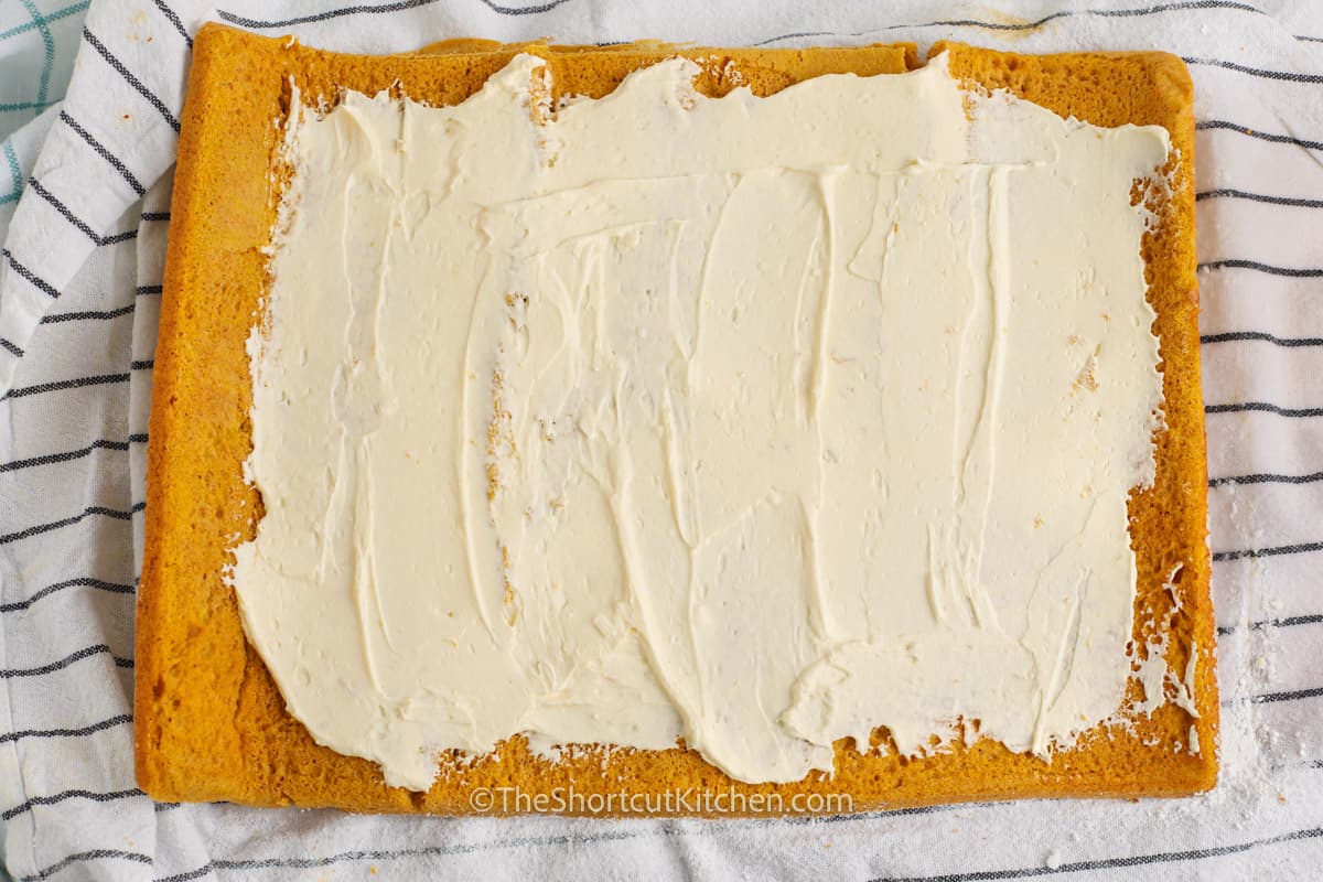 Cream cheese icing spread on Pumpkin Roll Cake