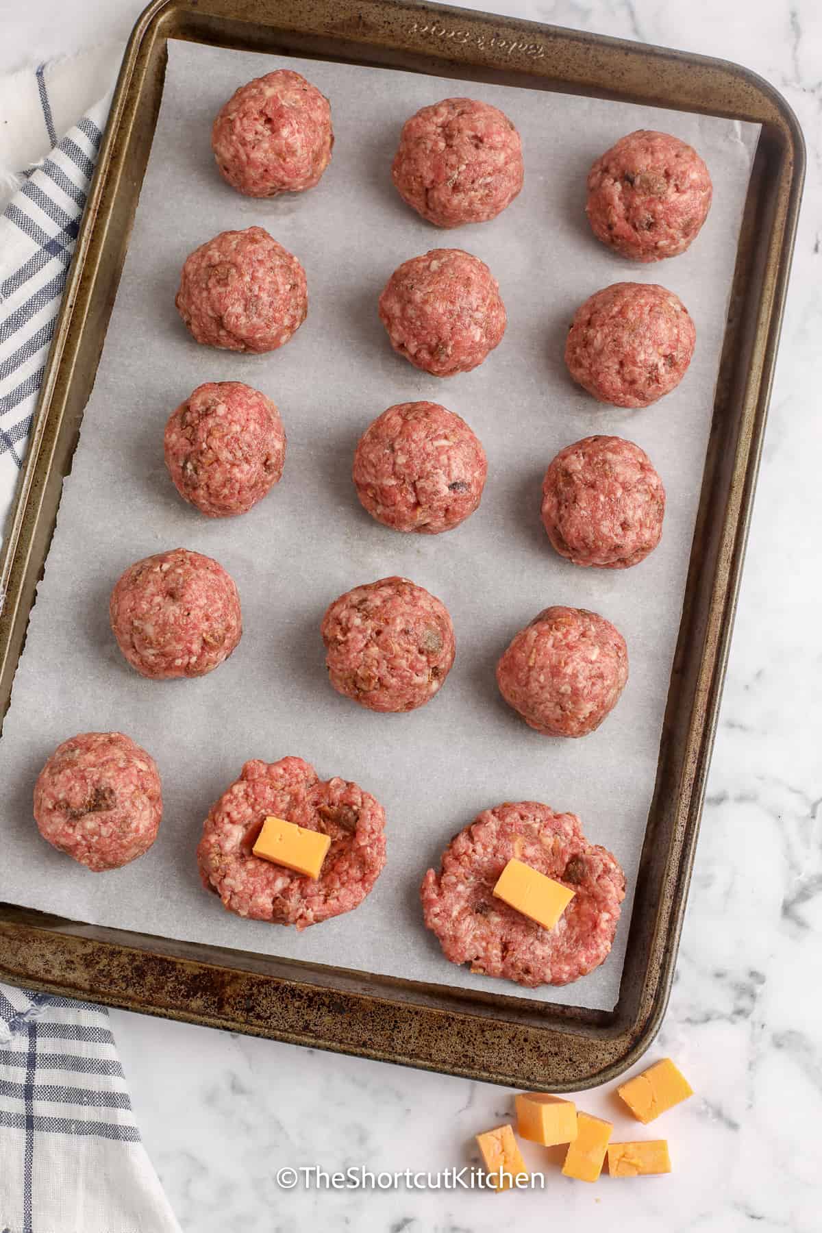 uncooked meatballs arranged on a tray, with two exposed with cheese cubes inside