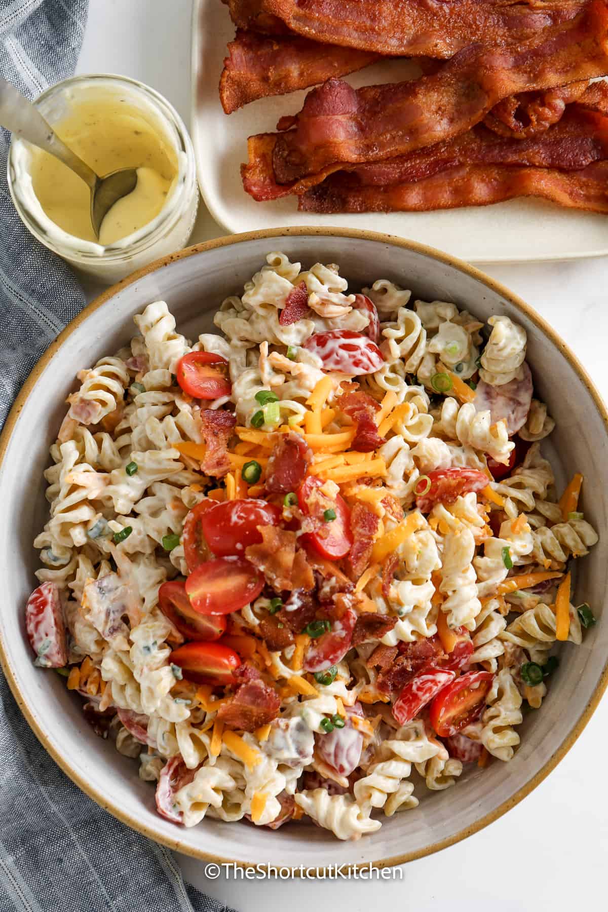 bacon ranch pasta salad in a bowl next to dressing and bacon