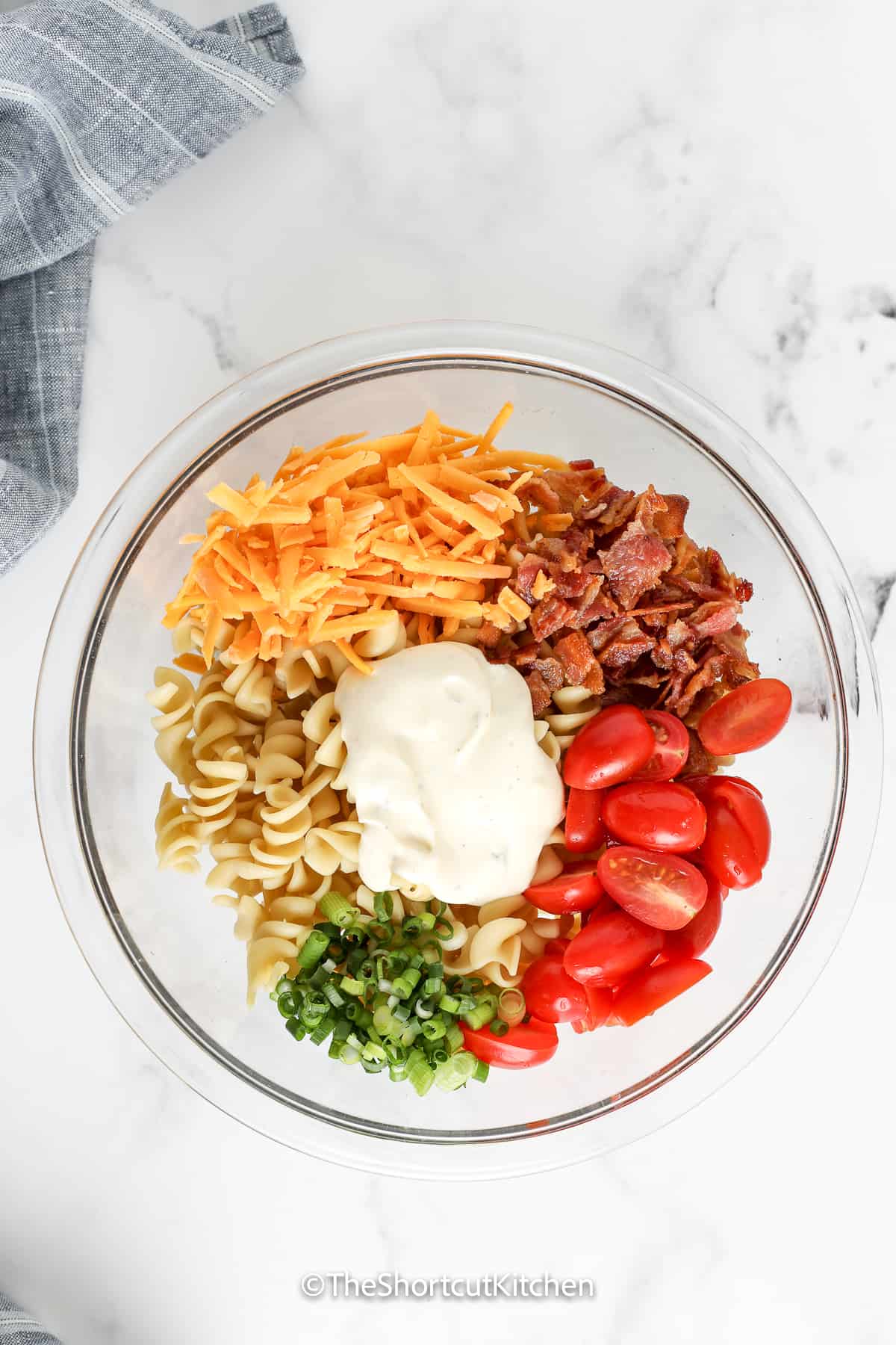 bacon ranch pasta salad ingredients in a bowl topped with dressing