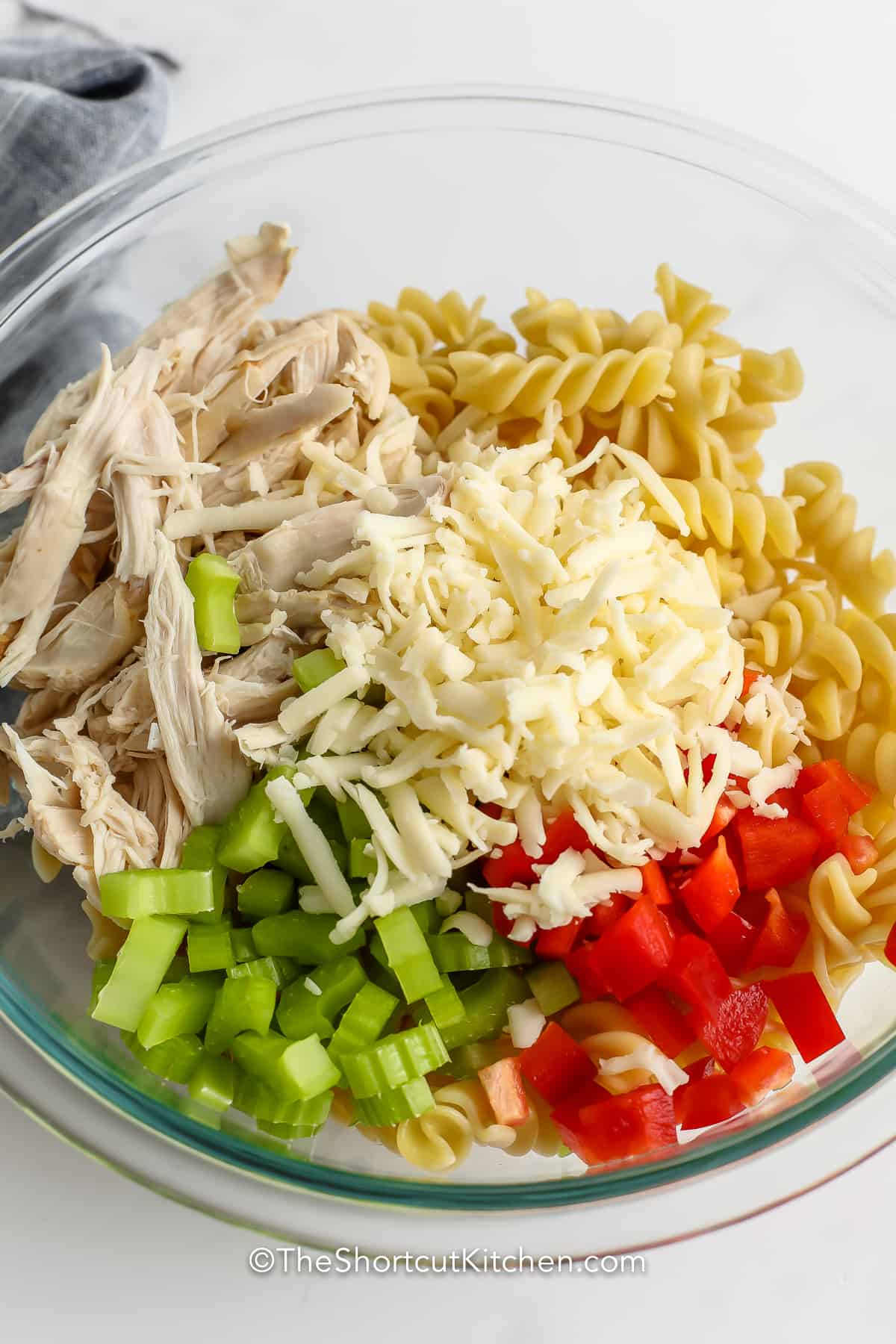 ingredients for buffalo chicken pasta salad in a clear mixing bowl, without the dressing.