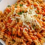 Buffalo Chicken Pasta Salad in a white serving bowl, garnished with green onion and parmesan cheese.