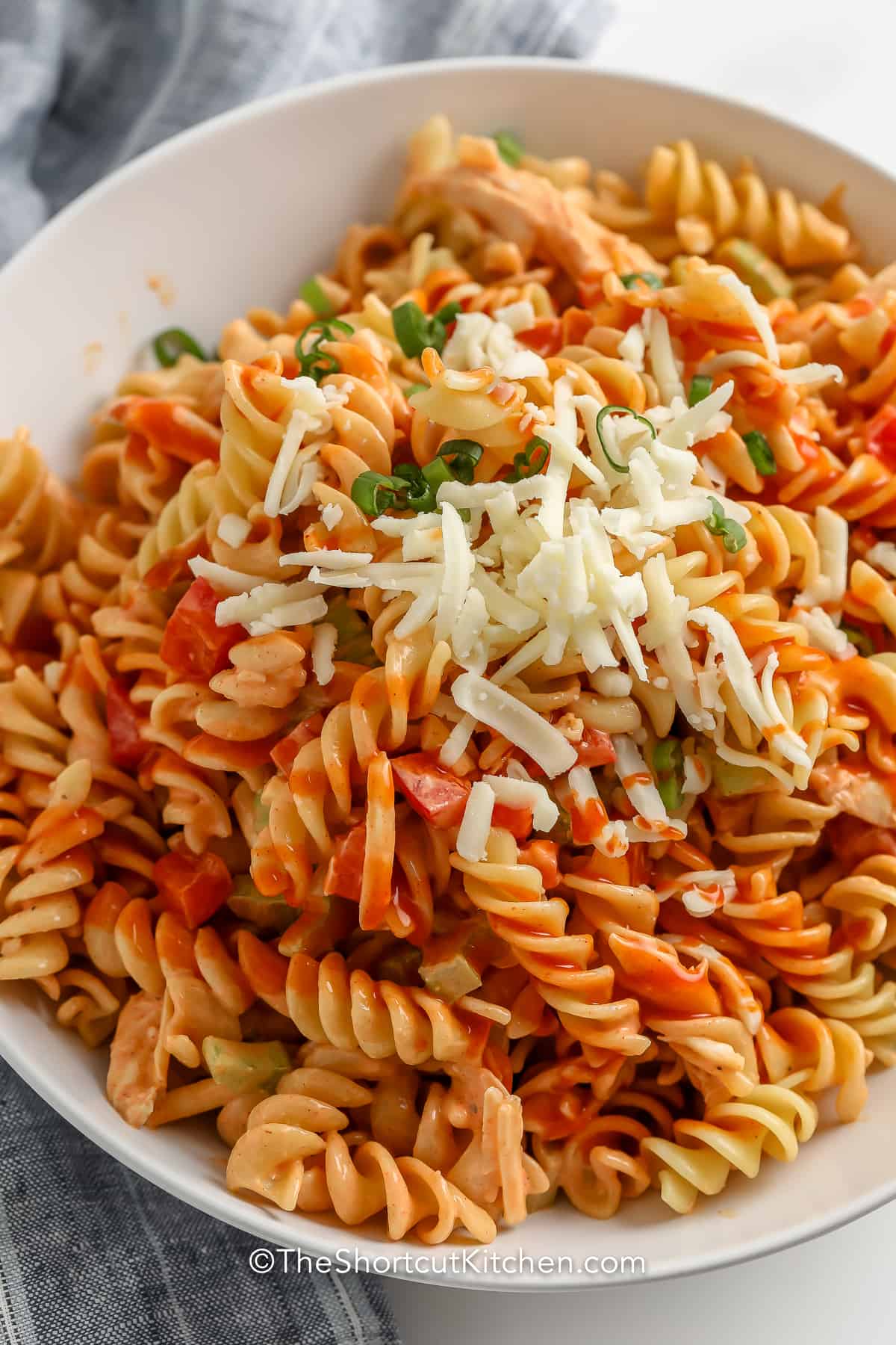 Buffalo Chicken Pasta Salad in a white serving bowl, garnished with green onion and parmesan cheese.