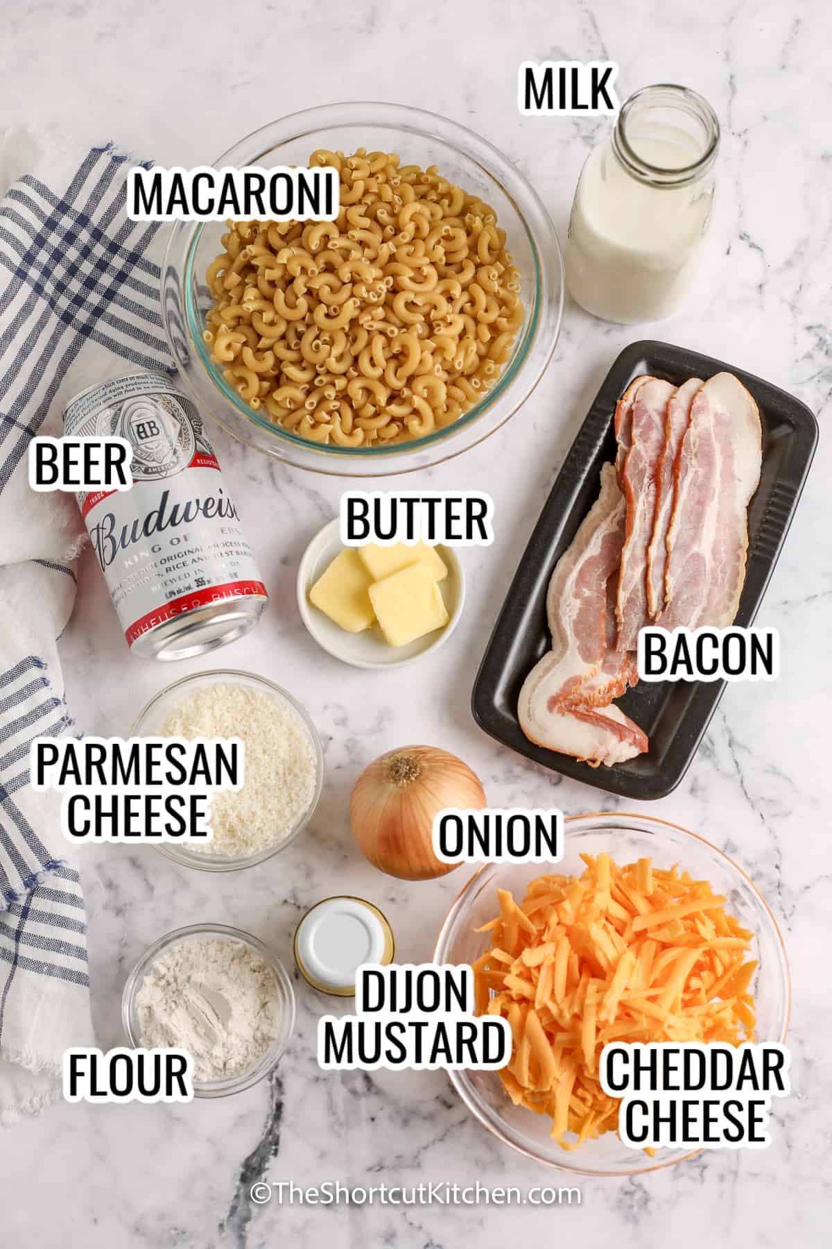 ingredients assembled to make beer mac and cheese including macaroni, beer, cheddar cheese, parmesan cheese, milk, bacon, onion, dijon mustard, flour, and butter