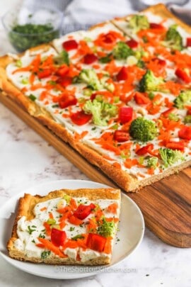 Cold Veggie Pizza slice on a plate with pizza in the back