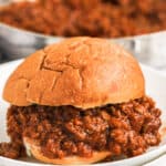 plated sloppy Joe with Homemade Sloppy Joe Sauce in a pan in the background