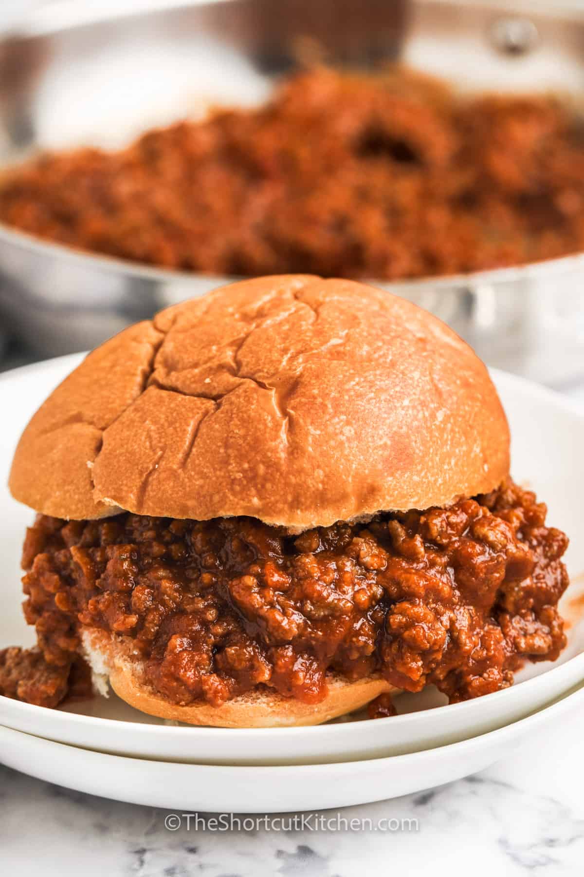plated sloppy Joe with Homemade Sloppy Joe Sauce in a pan in the background