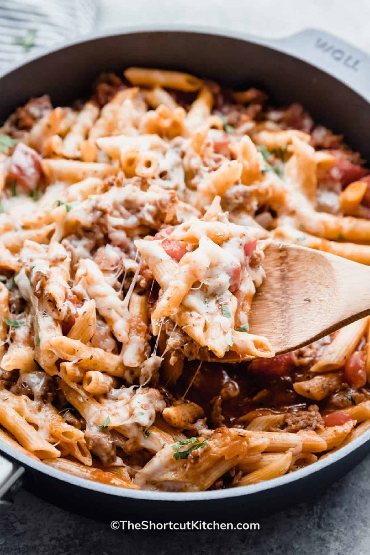 Italian Sausage Pasta in a skillet with a wooden spoon