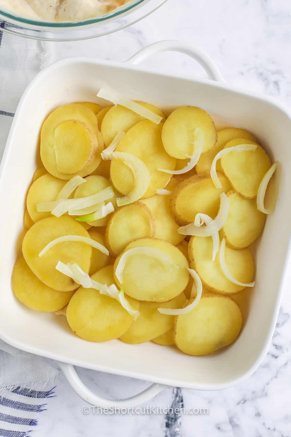 adding potato and onion layer to dish to make Easy Scalloped Potatoes and Ham