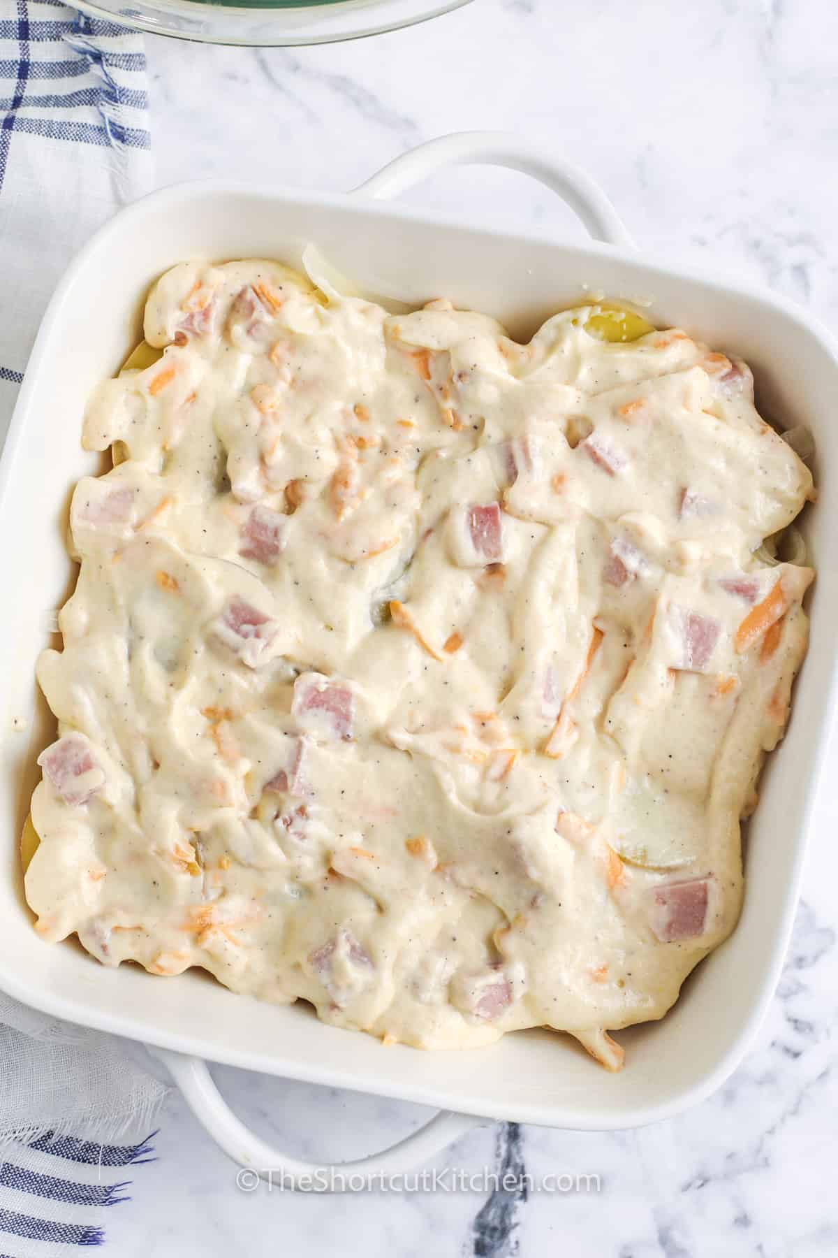 adding ham and cheese mixture on potatoes to make Easy Scalloped Potatoes and Ham