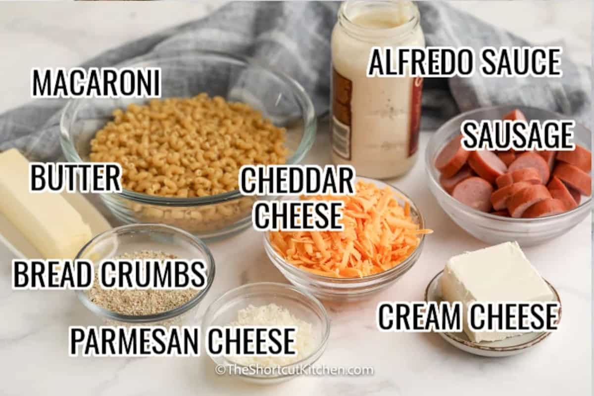 ingredients assembled to make creamy sausage mac and cheese, including macaroni, cheese, alfredo sauce, sausage, bread crumbs, and butter