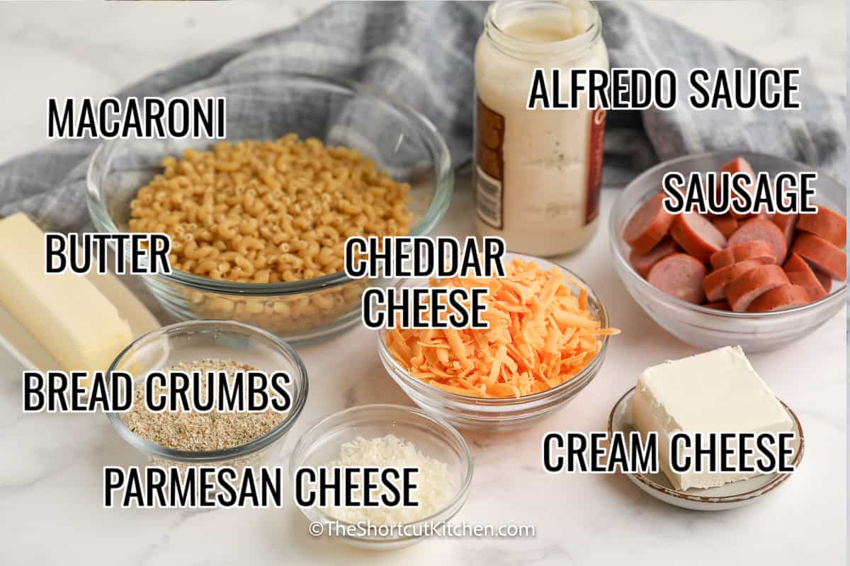 ingredients assembled to make creamy sausage mac and cheese, including macaroni, cheese, alfredo sauce, sausage, bread crumbs, and butter