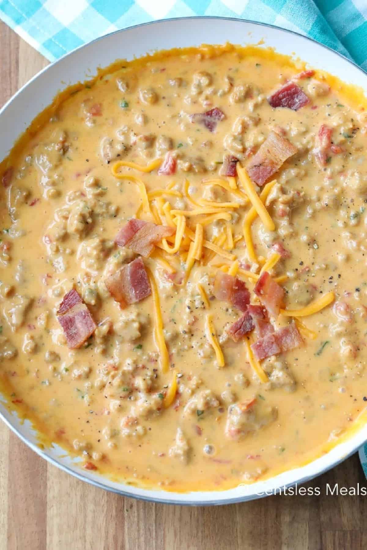 bacon cheeseburger dip in a white bowl garnished with bacon and cheese