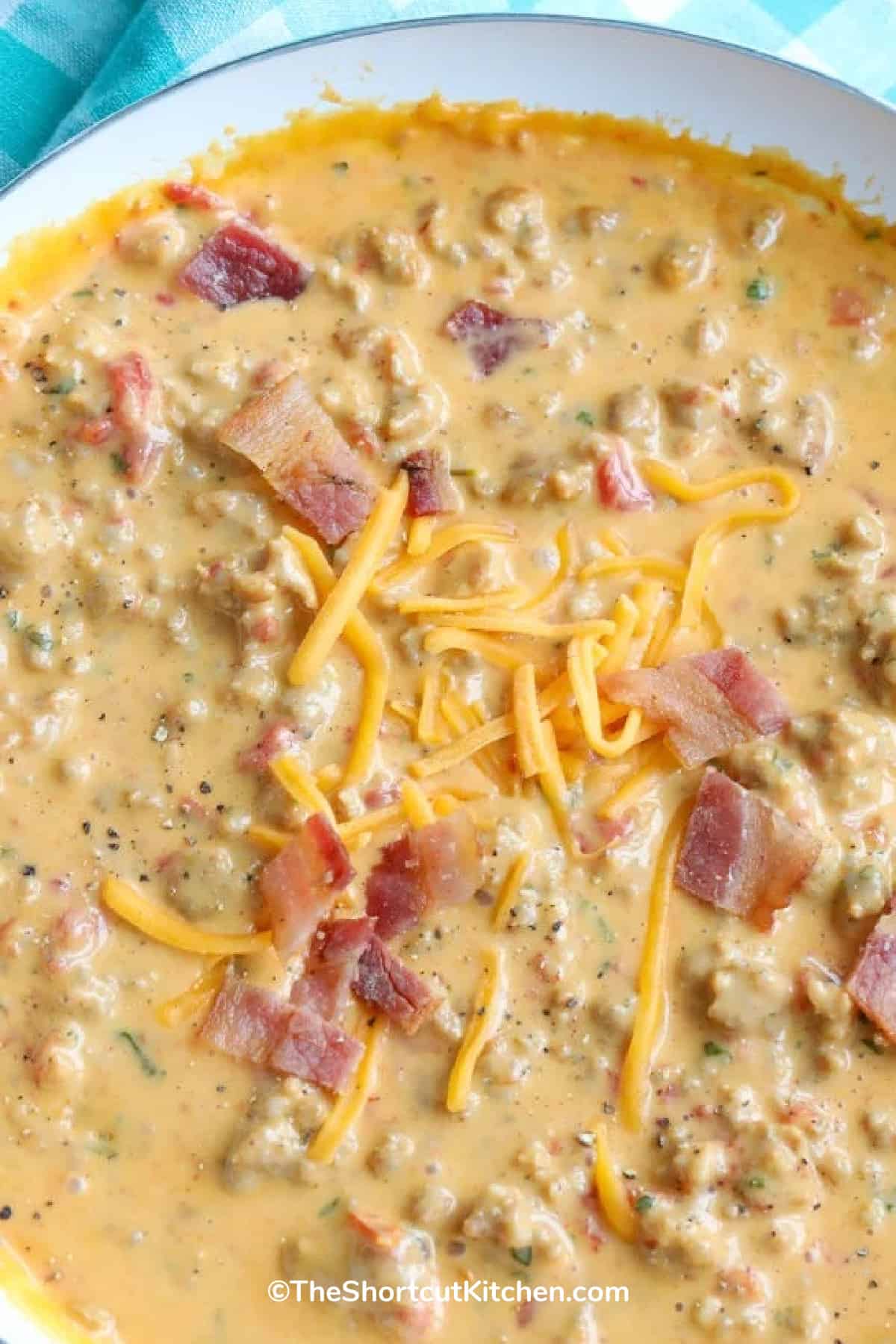 close up bacon cheeseburger dip in a white bowl garnished with bacon bits and grated cheese