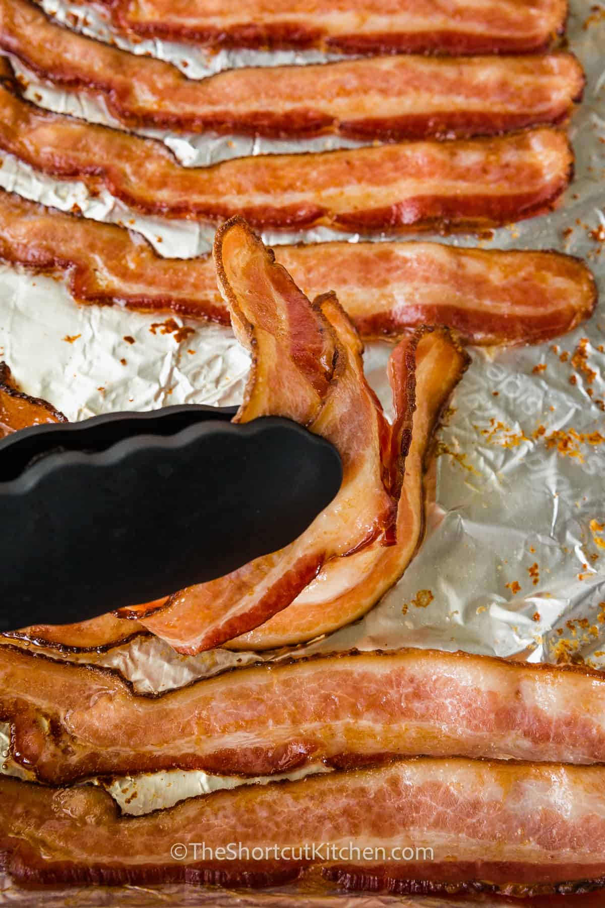 removing slices of cooked oven baked bacon from a foiled lined baking sheet