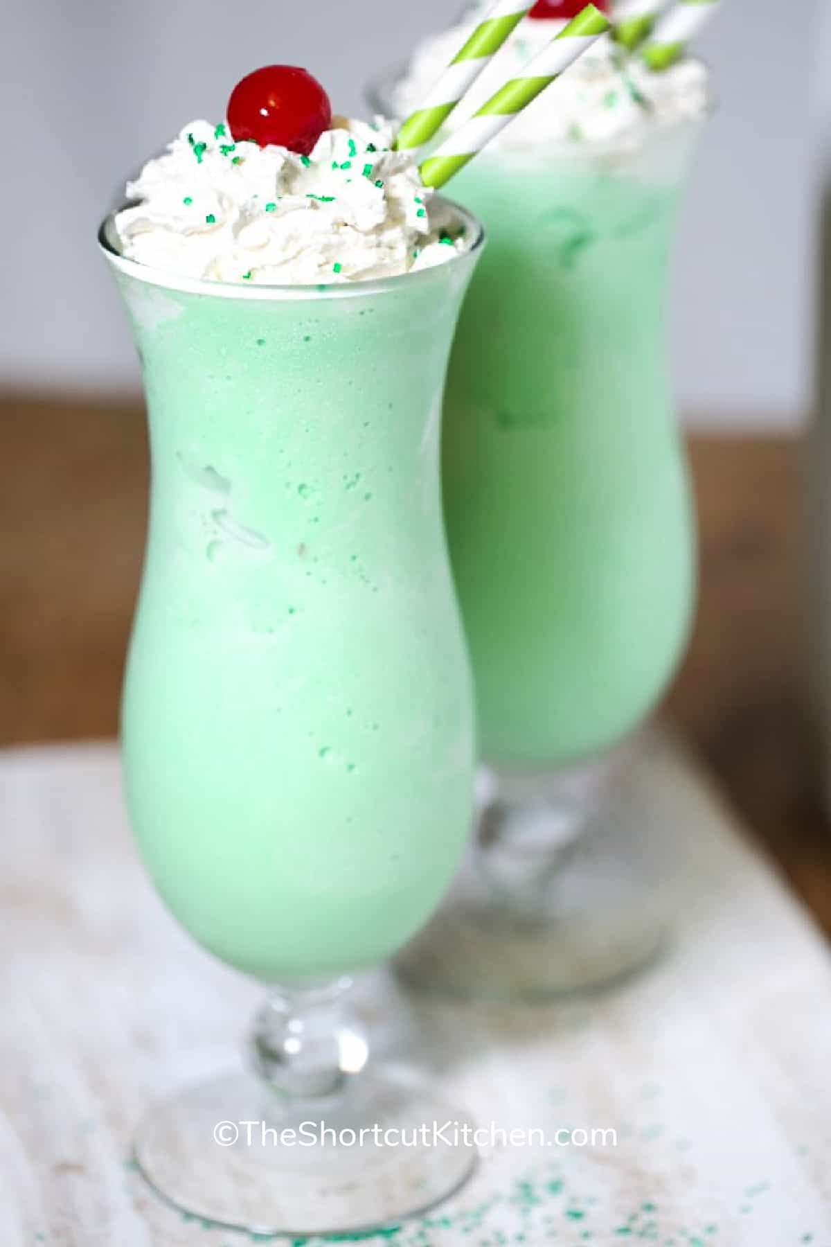 copycat shamrock shake recipe in a glass, topped with whipped cream, green sprinkles and a cherry