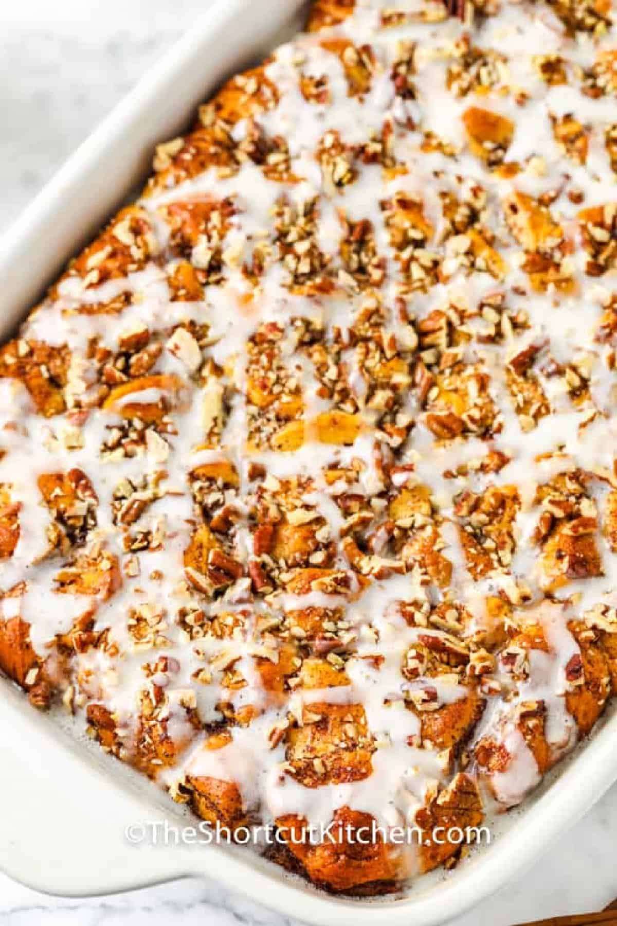 baked Cinnamon Roll French Toast Casserole in a white baking dish, with glaze on top