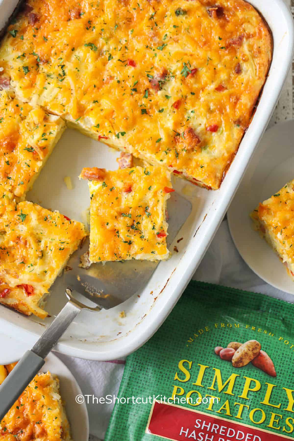 A slice of Hash Brown Breakfast Casserole being served from a white baking dish