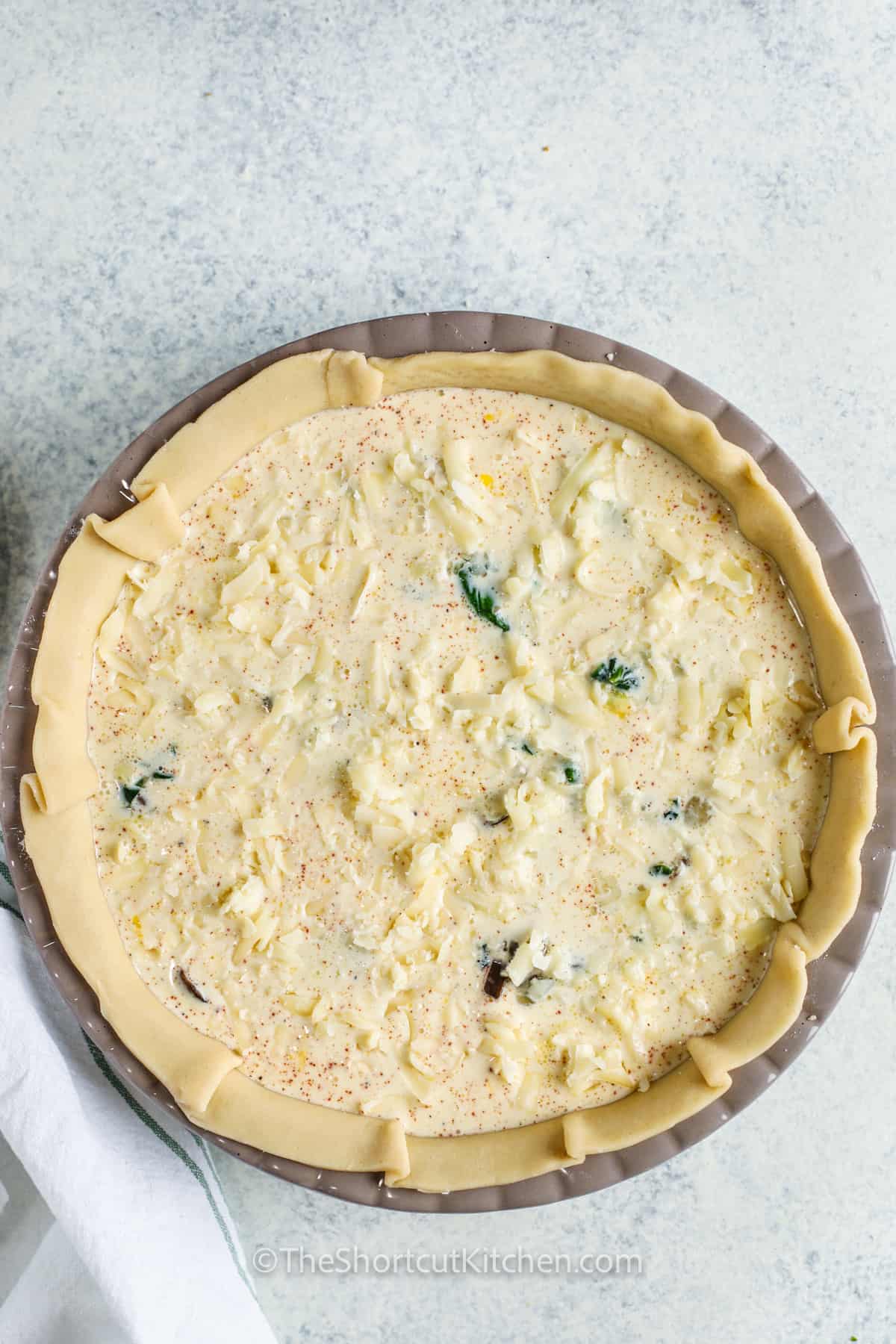 adding egg mixture with cheese to pie crust to make a Spinach Quiche Recipe