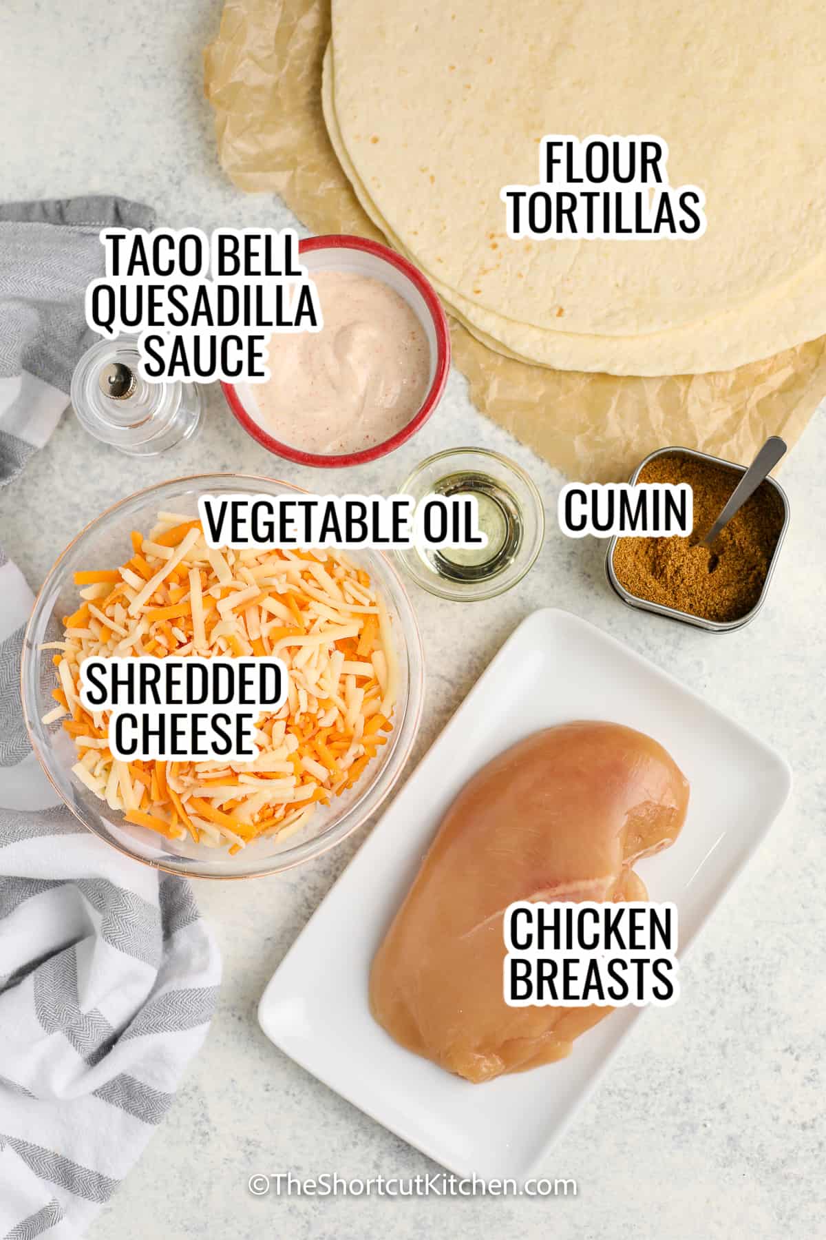 ingredients assembled to make copycat taco bell chicken quesadillas, including flour tortillas, quesadilla sauce, shredded cheese, chicken breasts, cumin, and vegetable oil