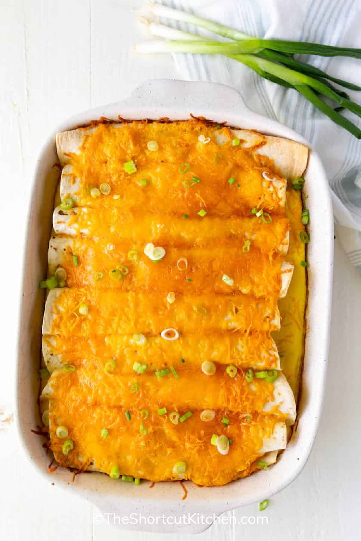 cheesy breakfast enchiladas recipe in a white baking dish with green onions on the side