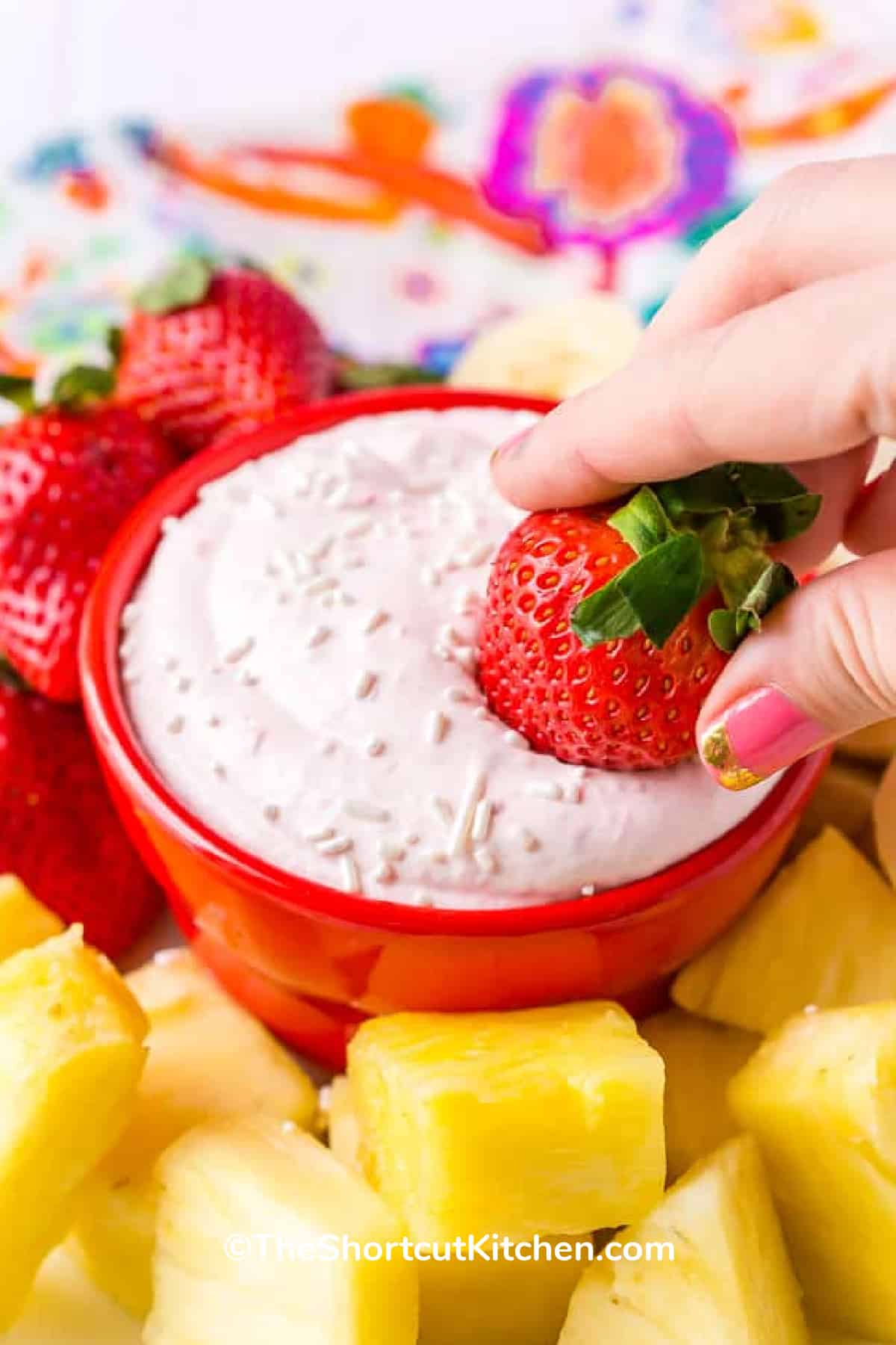 a strawberry being dipped into strawberry cream cheese fruit dip