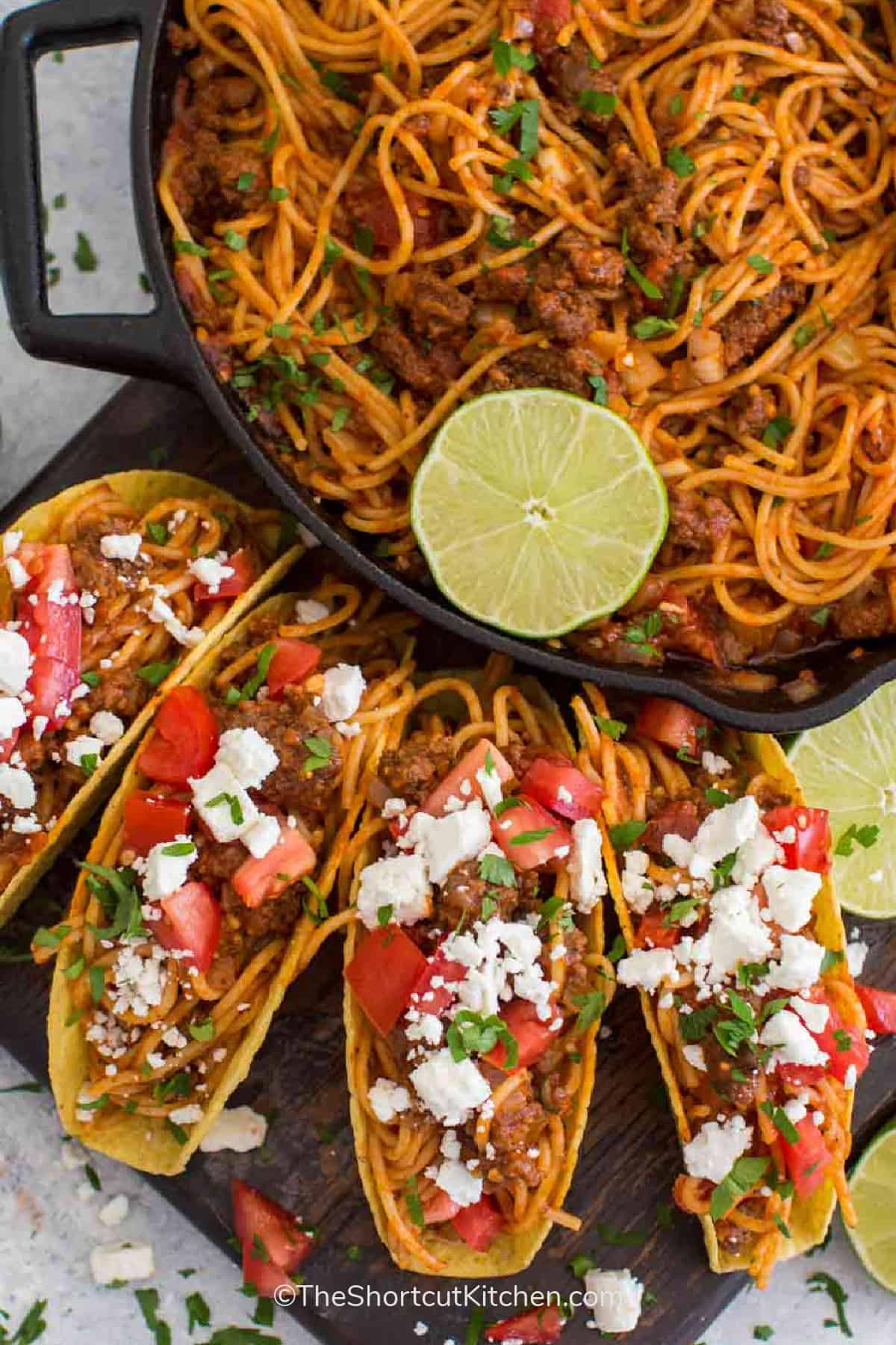 Four spaghetti tacos on a wooden board with spaghetti taco pasta in a skillet