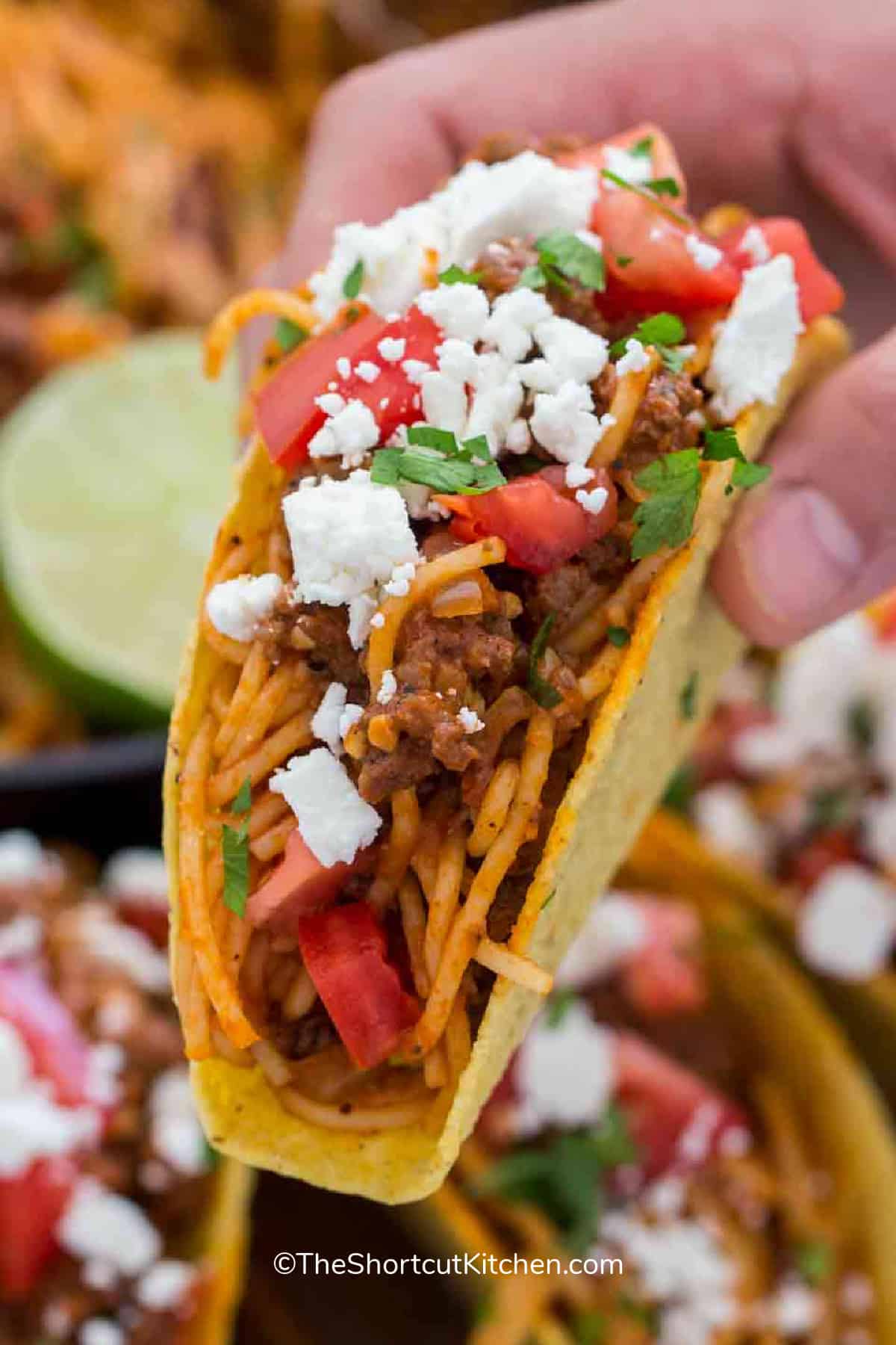 A spaghetti taco, garnished with feta, being held