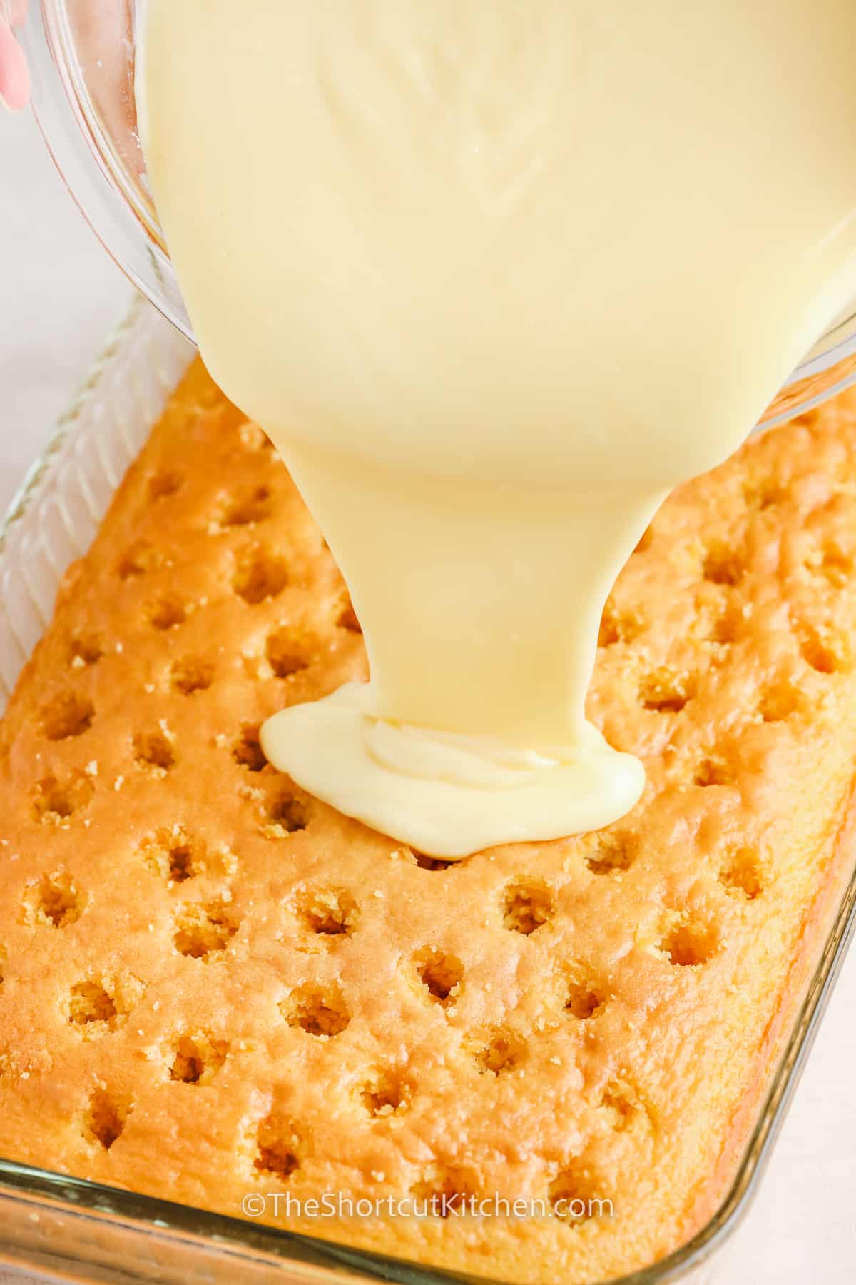 banana pudding being poured over a vanilla cake with holes in it.