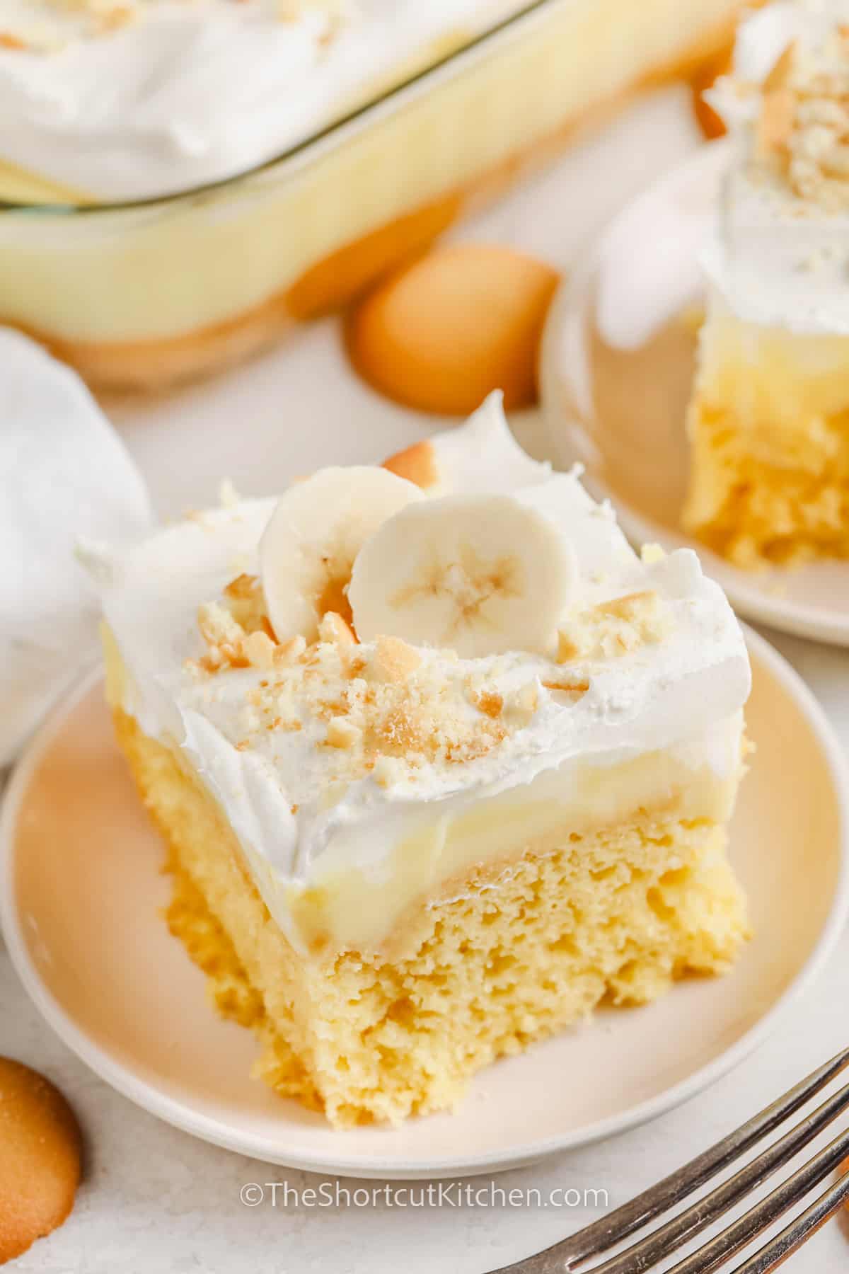 a slice of banana pudding poke cake topped with cookie crumbs and banana slices