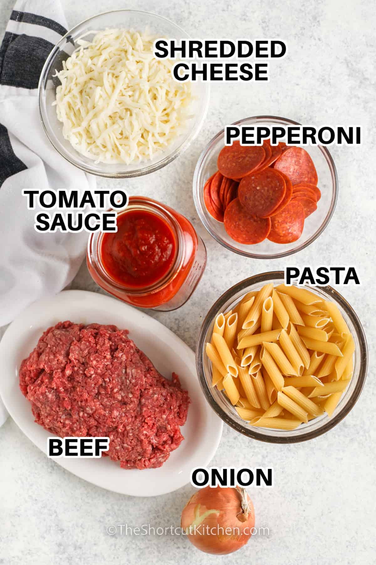 ingredients to make a pizza pasta bake: shredded cheese, pepperoni, tomato sauce, pasta, beef, and a onion