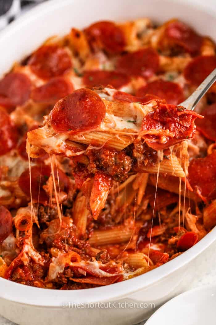 Pizza pasta bake being scooped out of a casserole dish