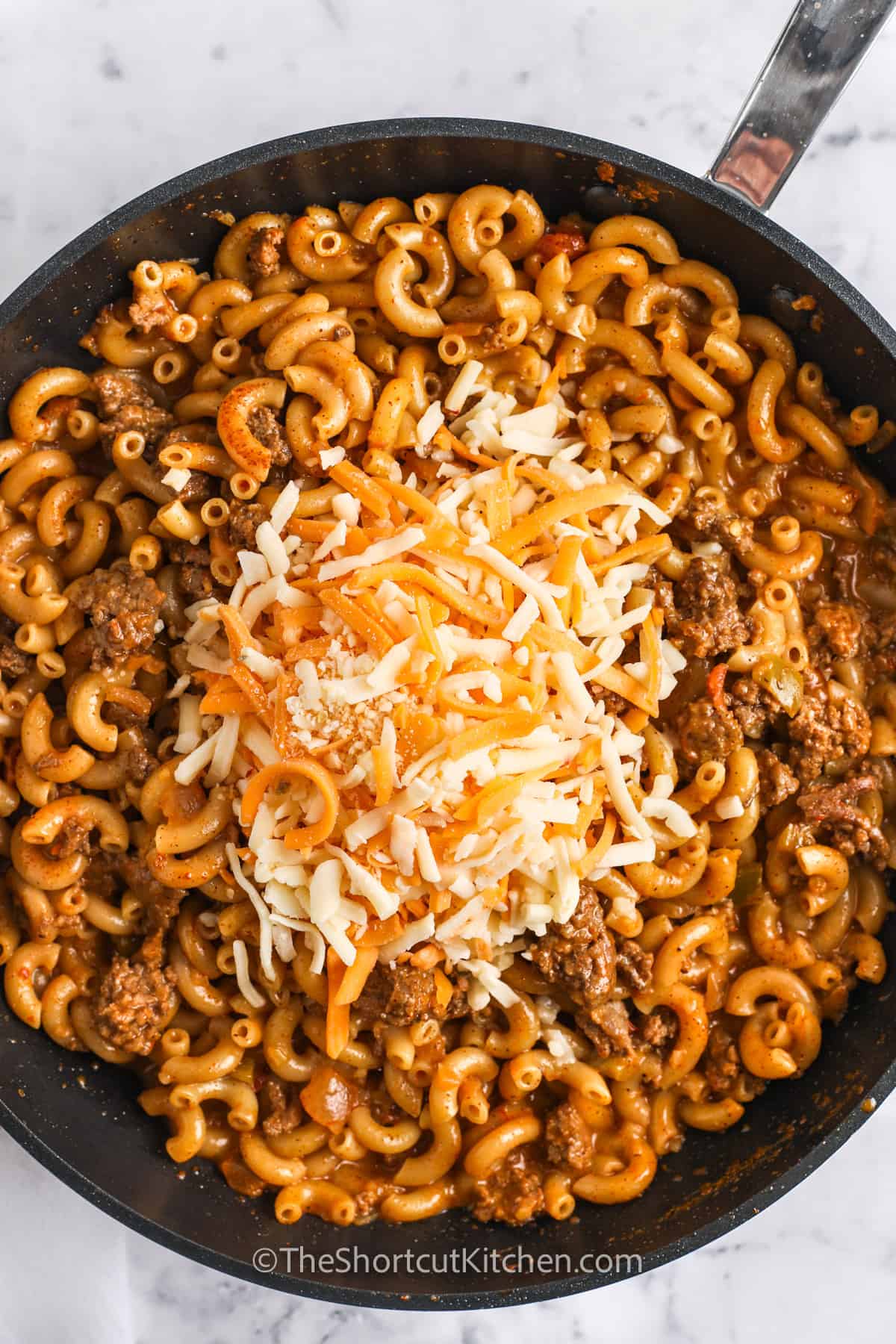 Cheese being added to the taco mac and cheese mixture in a frying pan