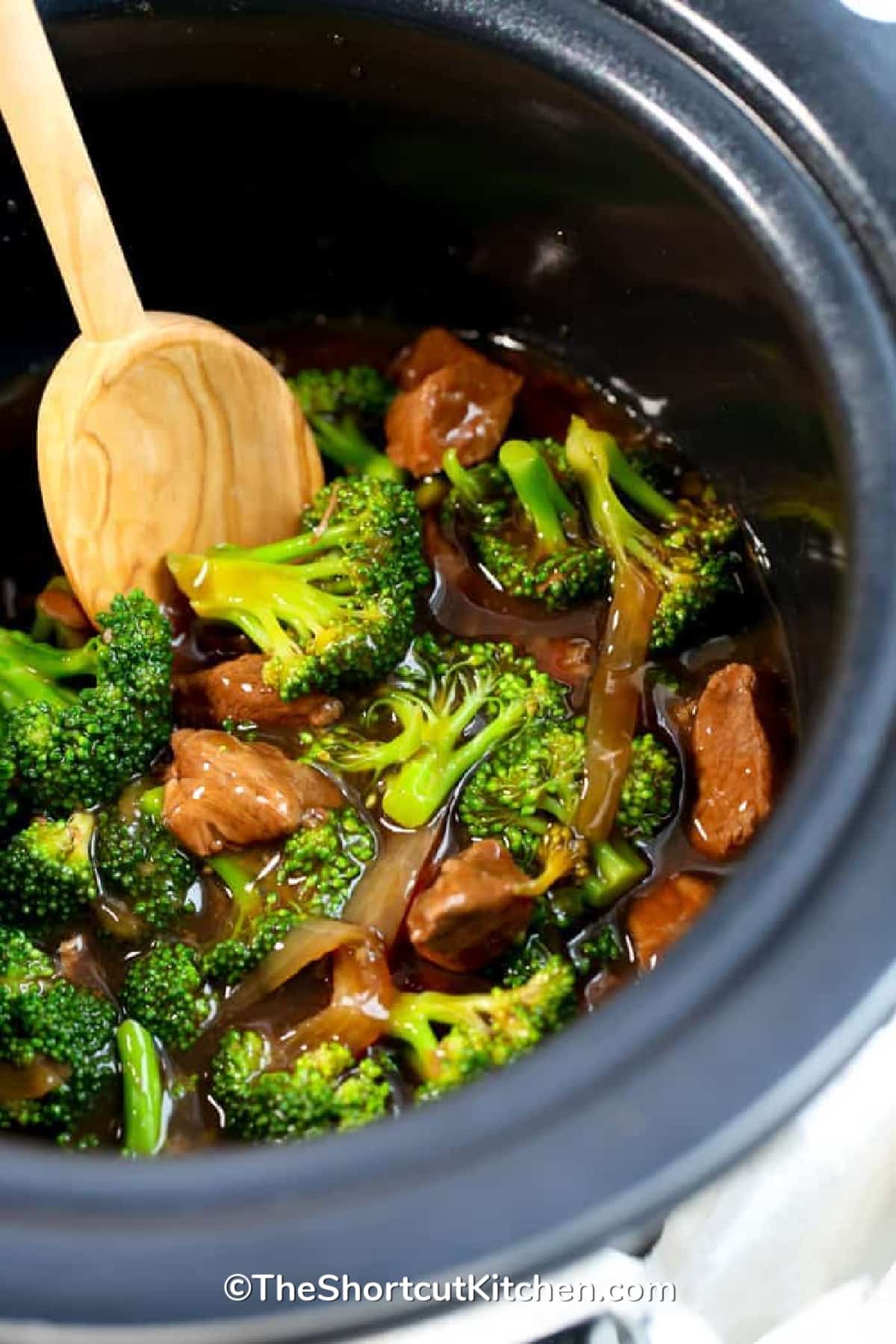 cooked Crockpot beef and broccoli in a slow cooker with a wooden spoon on the side