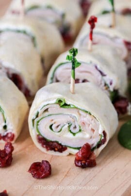 cranberry turkey pinwheels with festive toothpicks inserted in each on a wooden board