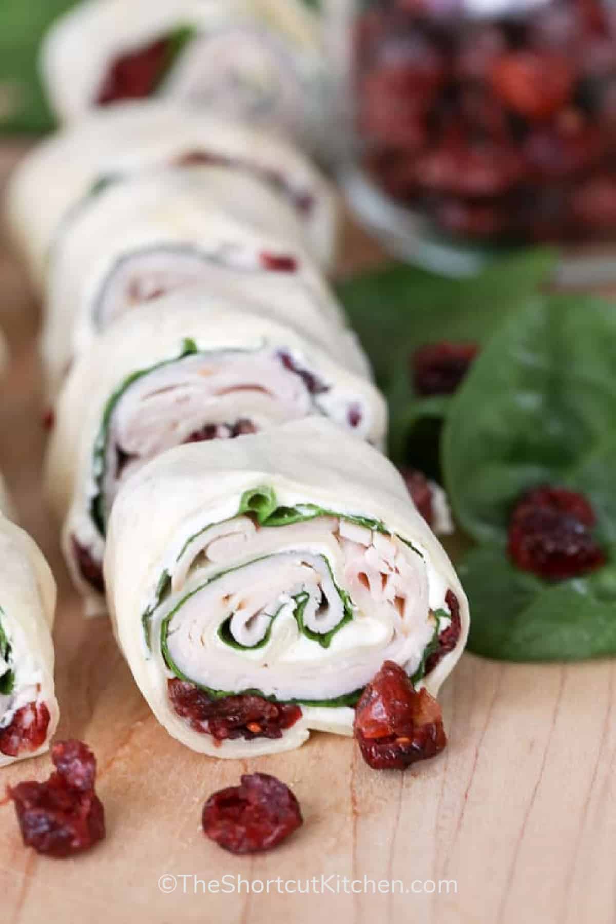 cranberry turkey pinwheels on a wooden board with cranberries and spinach leaves on the side