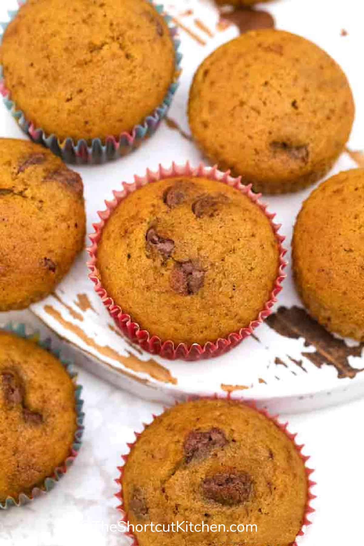 pumpkin chocolate chip muffins scattered on a white wooden board