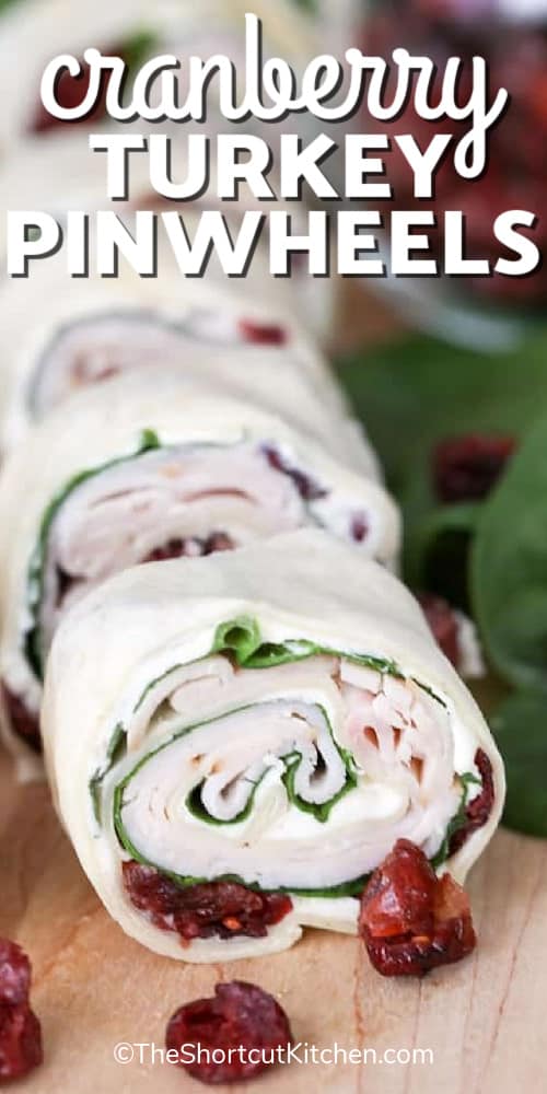 cranberry turkey pinwheels on a wooden board with cranberries and spinach leaves on the side, with a title