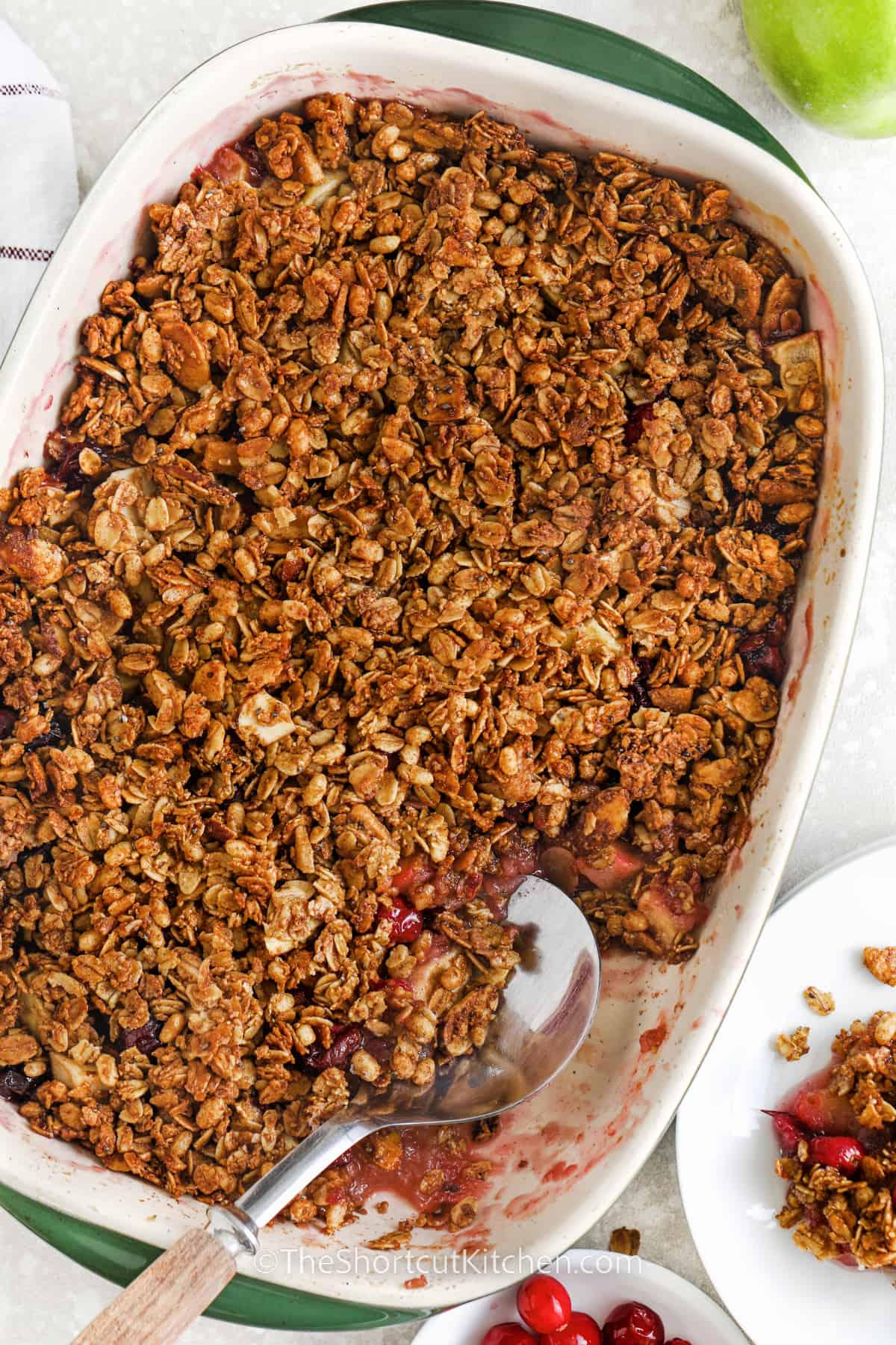apple cranberry crisp in a casserole dish with a spoon and a scoop taken out
