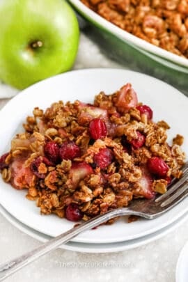 close up of apple cranberry crisp on a white plate with a fork