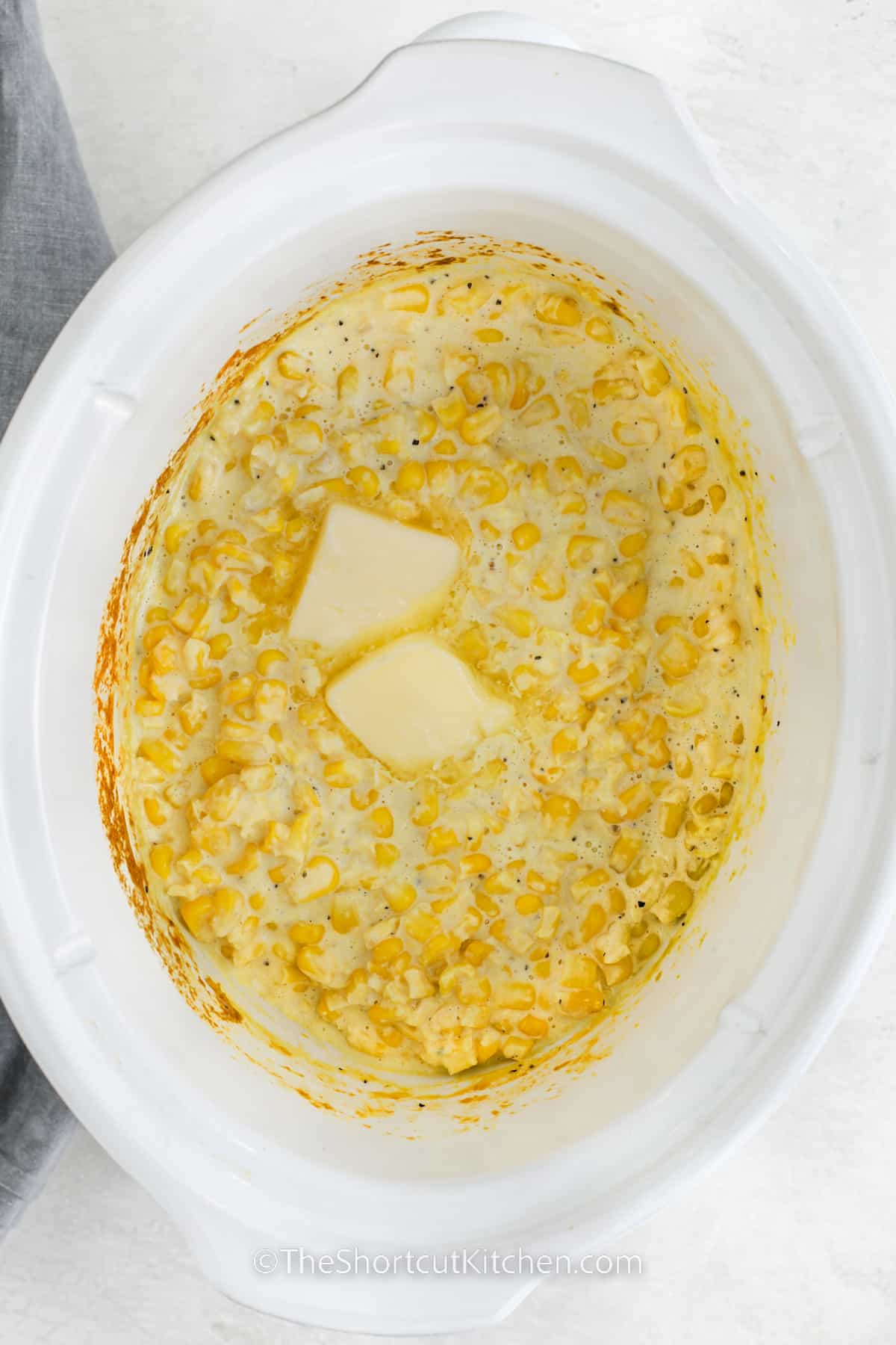Creamed corn prepared in a crockpot topped with two pats of butter