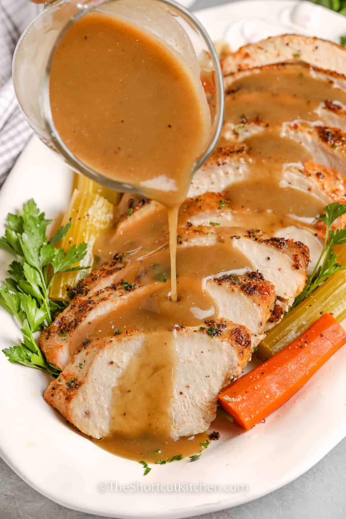 sliced crockpot turkey breast on a white serving dish with garnish and gravy being poured on