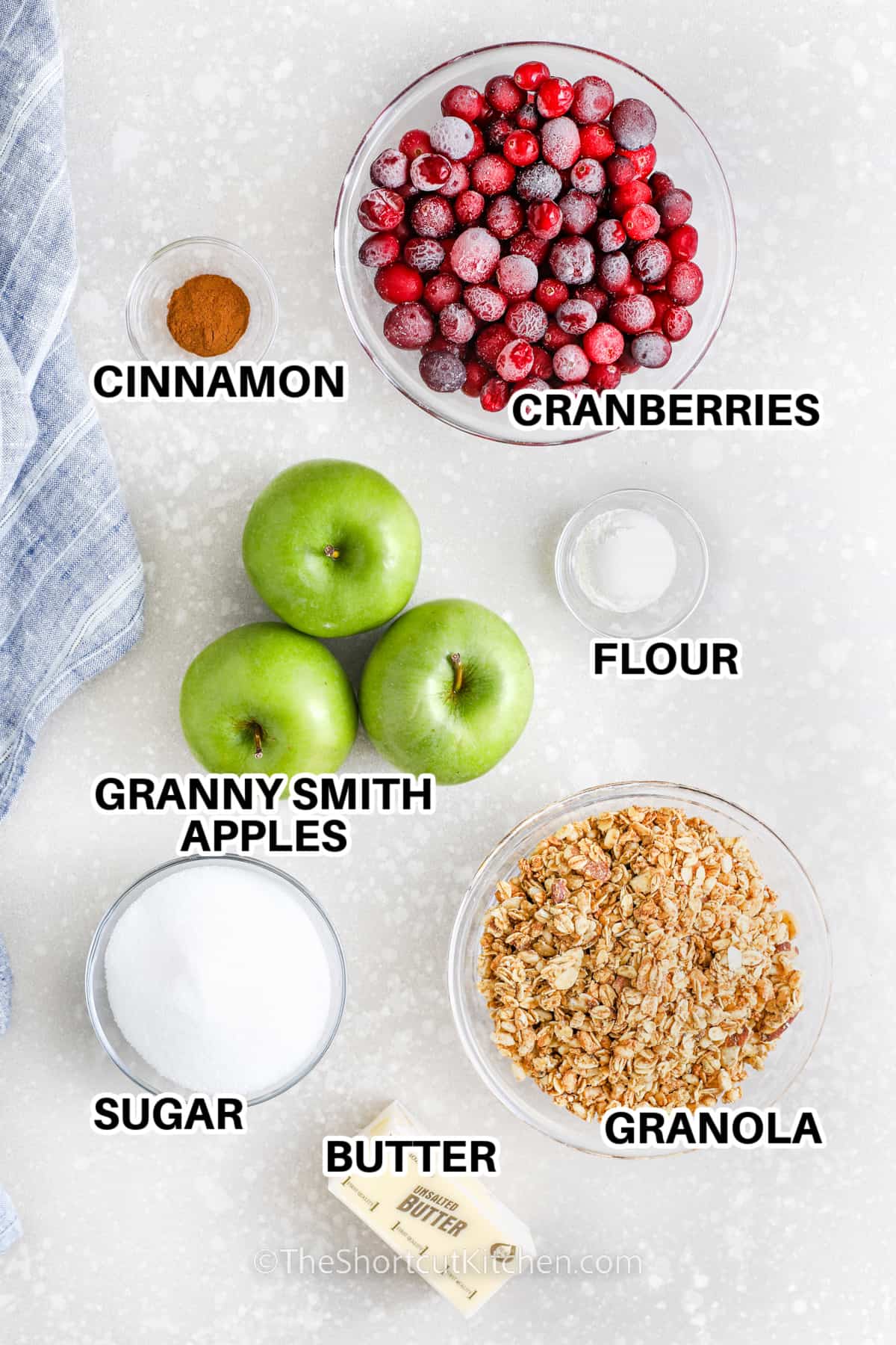 ingredients to make apple cranberry crisp including cranberries, cinnamon, granny smith apples, flour, butter, granola, sugar, and butter