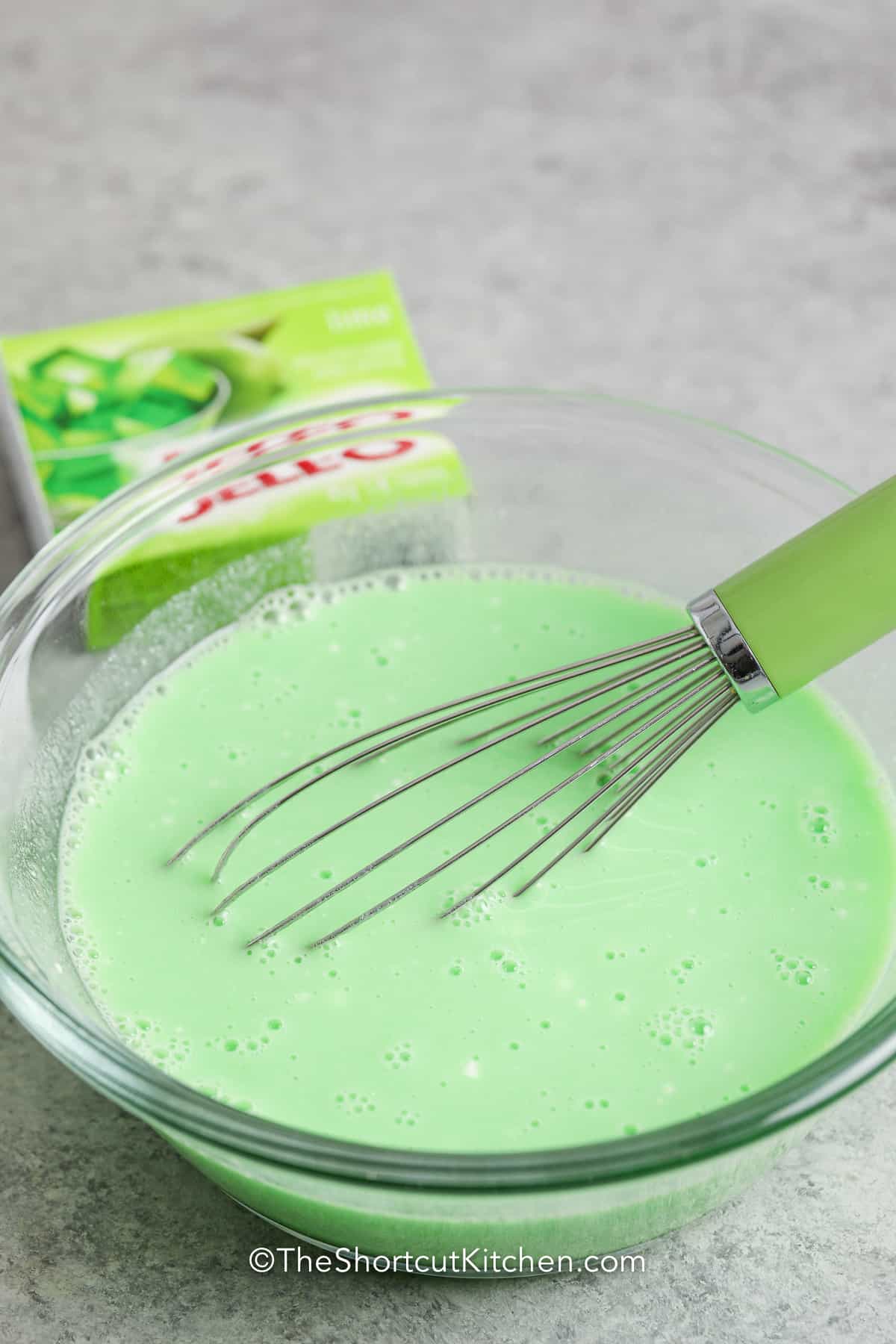 jello mixture in a glass bowl with a whisk for Lime Jello Salad