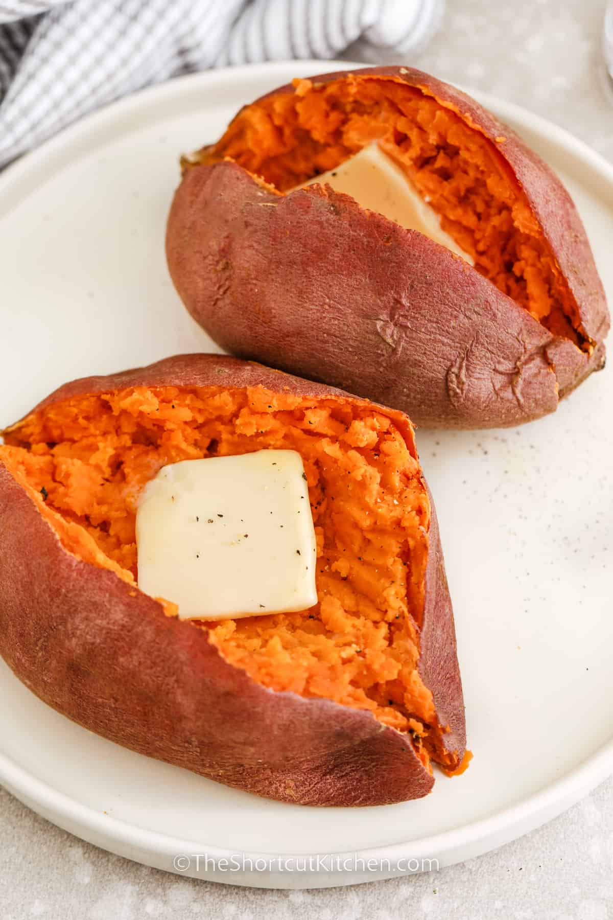 sweet potatoes split in half on a plate with butter on top