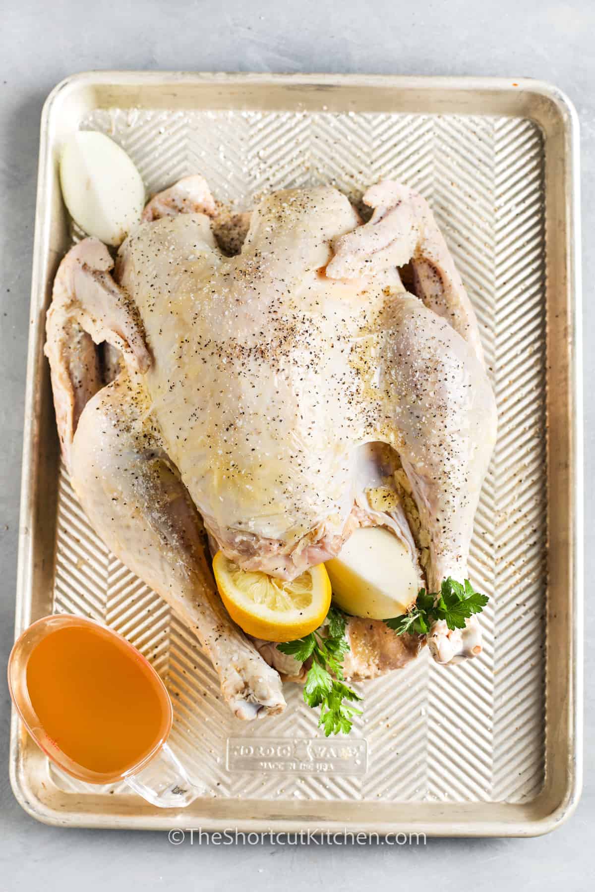 raw turkey on a baking sheet with onion and lemon inside