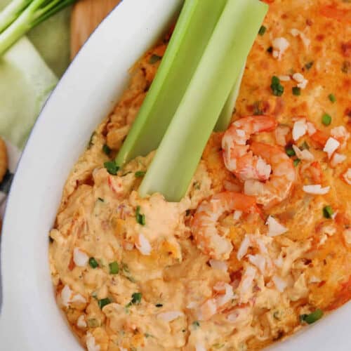 Shrimp dip in a white bowl with three celery sticks and shrimp on top