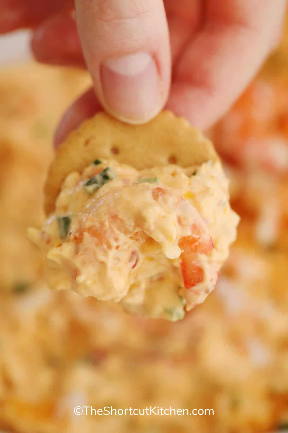 A cracker with shrimp dip on it being held.